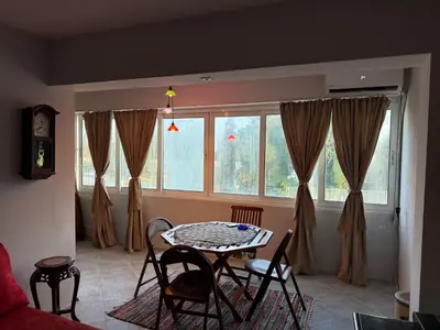 a living room with a table and chairs and windows at Emines apartman Budva in Budva