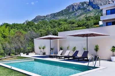 a swimming pool with chairs and umbrellas next to a building at Orange Tree Pool Villas - Sea View and Private Pool in Reževići
