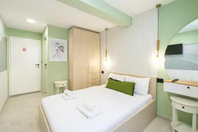 a small bedroom with a white bed and green walls at 7 Hills Rooms in Podgorica