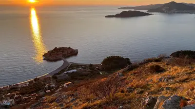 an island in the water with the sunset in the background at Penthouse Becici in Budva