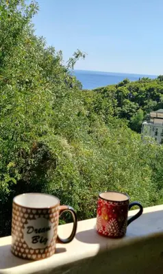two coffee mugs sitting on a window sill overlooking the ocean at Sun Apartment in Petrovac na Moru