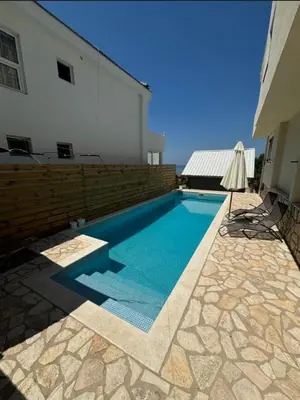 a swimming pool next to a building with an umbrella at B&K Villa Kruče Rooms in Ulcinj