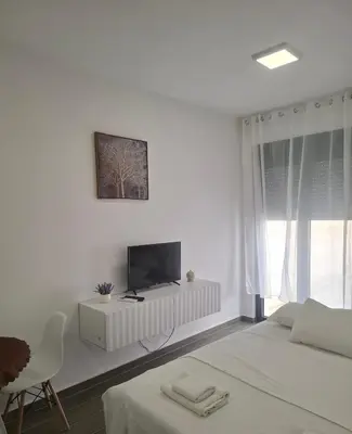 a white bedroom with a bed and a tv on a cabinet at ZEN Studio Apartman in Kotor