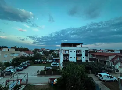 a white building with cars parked in a parking lot at Apartmani Monić in Ulcinj