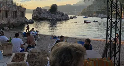 a group of people sitting on a beach near the water at Studio Sea View Steps to Przno beach w Parking Villa Olive in Pržno