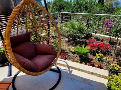 a wicker swing chair sitting on a patio with flowers at MiLA - Hladna Uvala in Utjeha