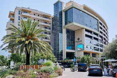 a tall building with a palm tree in front of it at Vista Mare Apartments in Budva