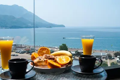 a table with a plate of food and two glasses of orange juice at Apartman Katica in Becici