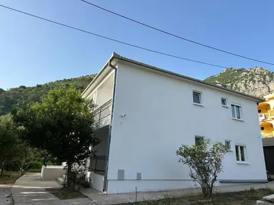 a white house with a mountain in the background at Apartmani Aki 5 in Bar