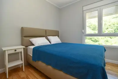 a bedroom with a bed with a blue blanket and two windows at Comfy one-bdr apartment Staša in Budva