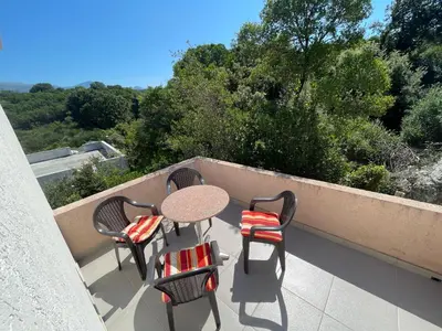 a table and chairs on a balcony with trees at Apartmani Ilić in Utjeha