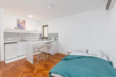 a white room with a bed and a kitchen at Cozy Studio Budva in Budva