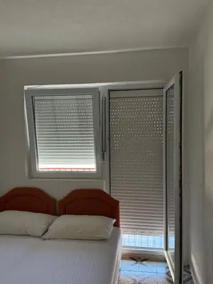 a bedroom with a bed and two windows with blinds at Tatjana apartman blue in Sutomore