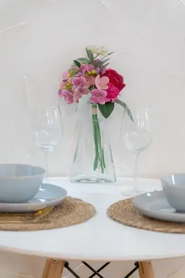 a vase with flowers in it on a table with glasses at Airport Apartments Una in Mitrovići