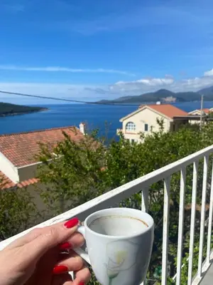 a woman holding a cup of coffee on a balcony at Bigova Peace Oasis in Bigovo