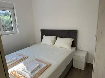 a small bedroom with a bed with white sheets and a window at Apartmani Aki 1 in Sutomore