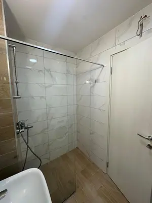 a bathroom with a glass shower and a sink at Modern 2BR - Smart TV and WiFi in Podgorica