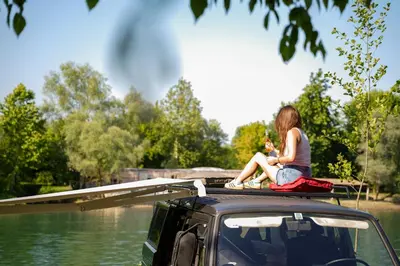 a woman sitting on the roof of a vehicle next to the water at Camperlife Montenegro in Podgorica