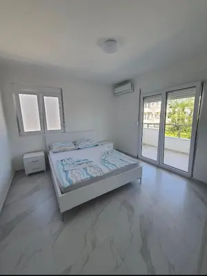 a white bedroom with a bed and a large window at Apartmani Ajla in Donji Štoj