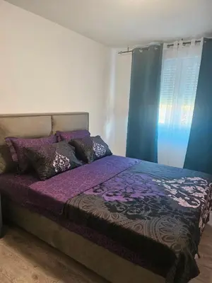 a bedroom with a bed with purple sheets and blue curtains at Apartman Mateo in Cetinje