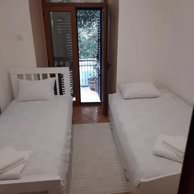 two beds in a room with a door to a balcony at Apartman HOME Kotor in Kotor