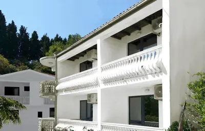 a white building with windows and trees in the background at Apartmani Ulcinj Mirza in Ulcinj