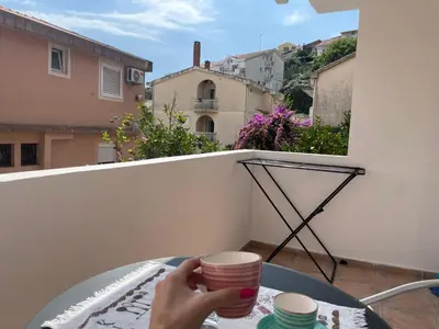a person holding two cups on a table on a balcony at Walk to the Sea-1 bedroom BUDVA in Budva