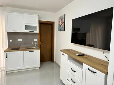 a kitchen with white cabinets and a flat screen tv at Студия в Добра Вода in Dobra Voda