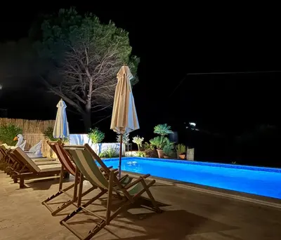 two chairs and umbrellas next to a swimming pool at night at Casa del Sol Zagora in Zagora