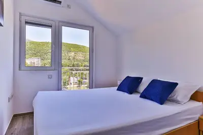 a white bed with blue pillows in a room with a window at Palm Park Budva in Budva