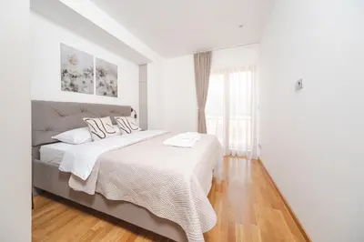 a white bedroom with a large bed and wooden floors at Autentica Apart in Cetinje