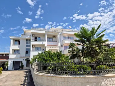 a white building with a palm tree in front of it at Apartments Yll 3 in Ulcinj