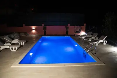 a swimming pool at night with chairs and a table at Blue Escape in Danilovgrad