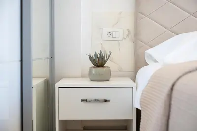 a white nightstand with a plant on it next to a bed at OliveRock Apartments - Hladna Uvala in Kruče