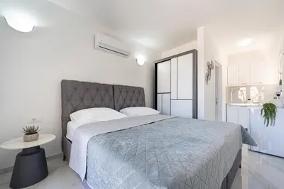 a white bedroom with a large bed and a table at OliveRock Apartments - Hladna Uvala in Kruče