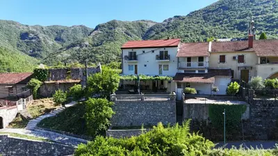 a house in a village with mountains in the background at Riječki grad Apartments in Rijeka Crnojevića