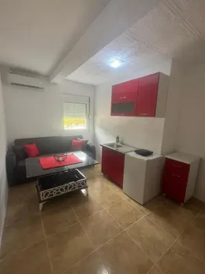 a living room with a couch and a kitchen with red cabinets at Apartmani Đurović - Sutomore in Bar