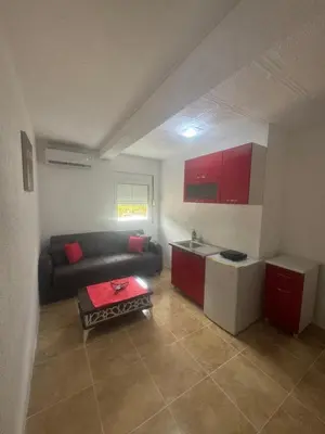 a living room with a couch and a kitchen with red cabinets at Apartmani Đurović - Sutomore in Bar