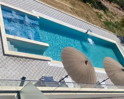 an overhead view of a swimming pool with two umbrellas at sea and sun luxury apartment in Ulcinj