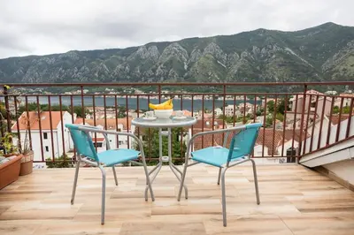 a table and chairs on a balcony with mountains at Bay View Apartment in Kotor