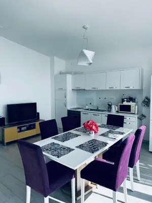 a white kitchen with a table and purple chairs at SF Apartments Lux in Dobra Voda