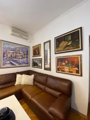a living room with a brown leather couch and framed pictures at Stylish Charm Downtown in Podgorica