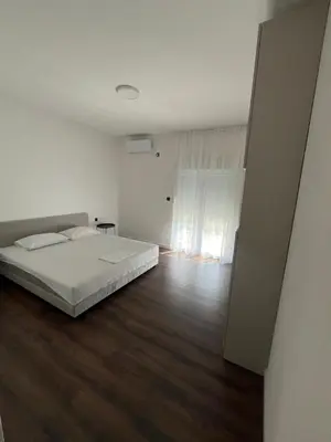 a white bedroom with a bed and a wooden floor at Lola Guest House in Budva