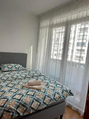 a bedroom with a bed with a quilt and two windows at Apartman Mina in Podgorica