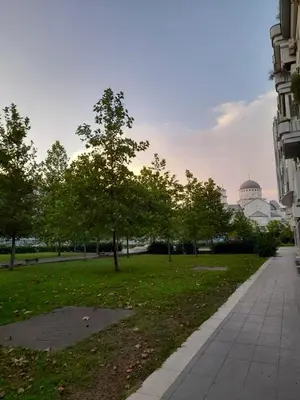 a park with trees and a building and a sidewalk at Apartman Mina in Podgorica