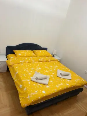 a bed with a yellow comforter with slippers on it at Apartman Mina in Podgorica