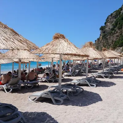 a group of people sitting on the beach under straw umbrellas at Seaview Retreat Reževići in Reževići