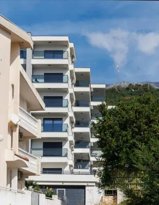 a white apartment building with a hill in the background at HELEN LUX Apartments in Dobra Voda