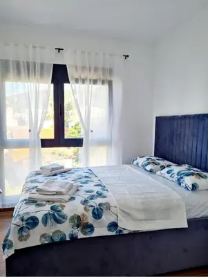 a bed with a blue headboard and a window at HELEN LUX Apartments in Dobra Voda