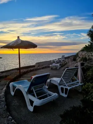 two lounge chairs and an umbrella next to the water at HELEN LUX Apartments in Dobra Voda